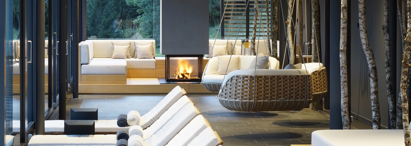 Blick durch einen Ruheraum im Spa mit weißen Liegen und einem Kamin im Hintergrund.