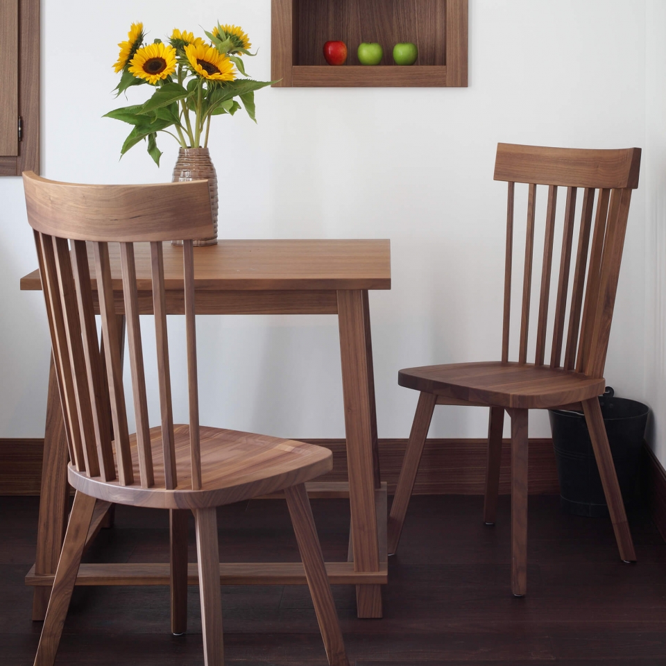 Aufnahme einer Sitzgruppe im Hotel Das Tegernsee mit zwei dunkelbraunen Holzstühlen und einem kleinen Holztisch auf dem frische Sonnenblumen in einer Vase stehen.
