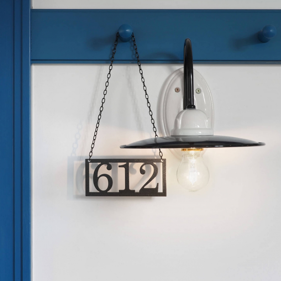 Detailaufnahme einer modernen, schwarz-weißen Wandlampe, neben dem ein Metallschild mit der Zimmernummer 612 hängt.