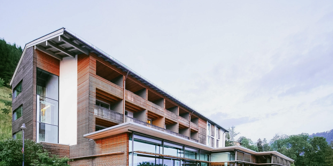 Aufnahme von außen vom Haus Wallberg im Hotel Das Tegernsee, mit Holzelementen an der Außenfassade und vielen Balkonen.