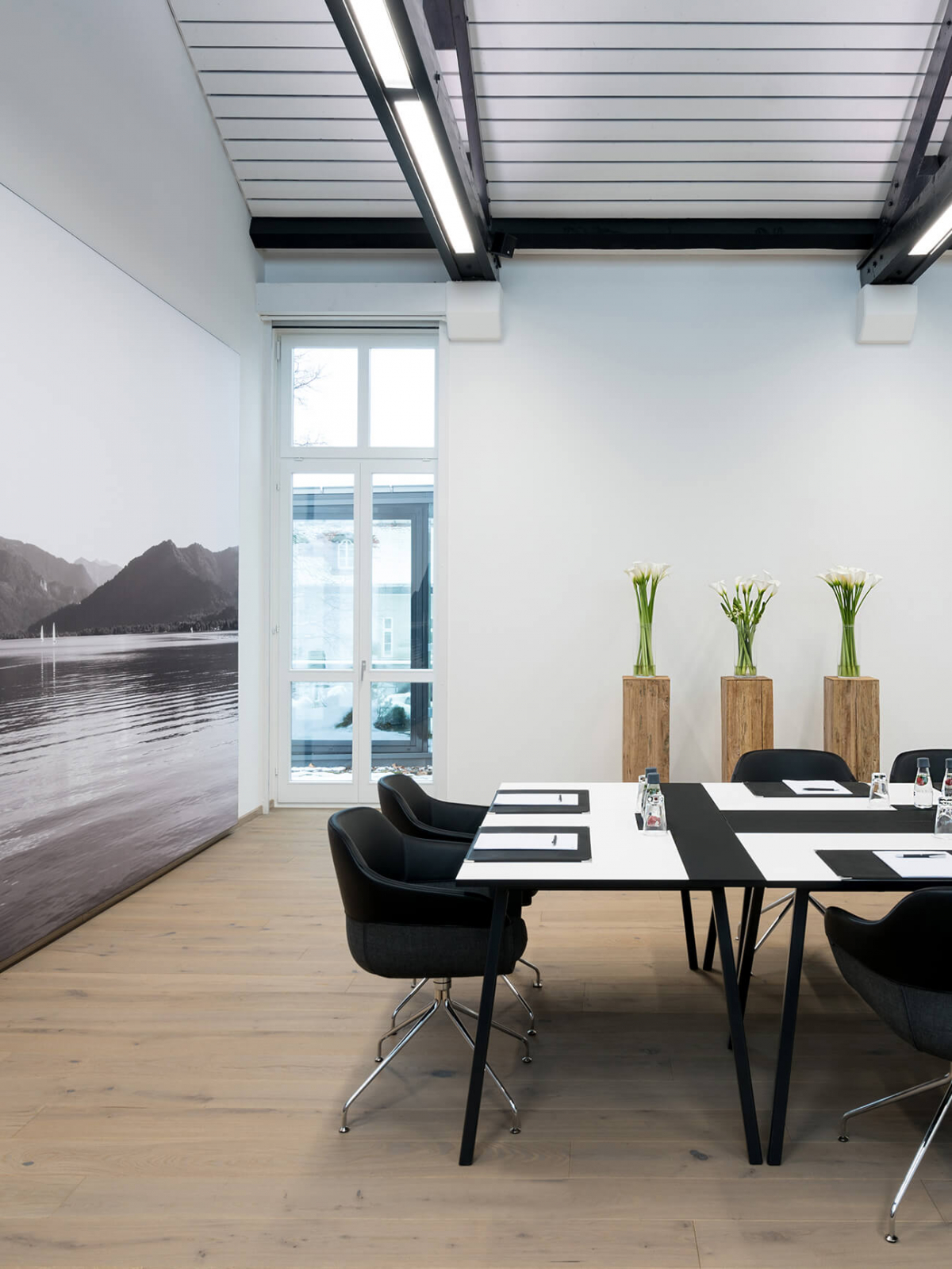 Aufnahme im Tagungsraum mit mehreren schwarzen Polsterstühlen, die an schwarz-weißen Tischen in Blockform angeordnet sind.